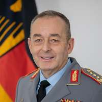 Carsten Breuer schaut in eine Kamera, hinter ihm ist aufgestellt die Flagge Deutschlands.