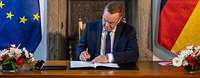 Boris Pistorius is signing a document while sitting at a desk.